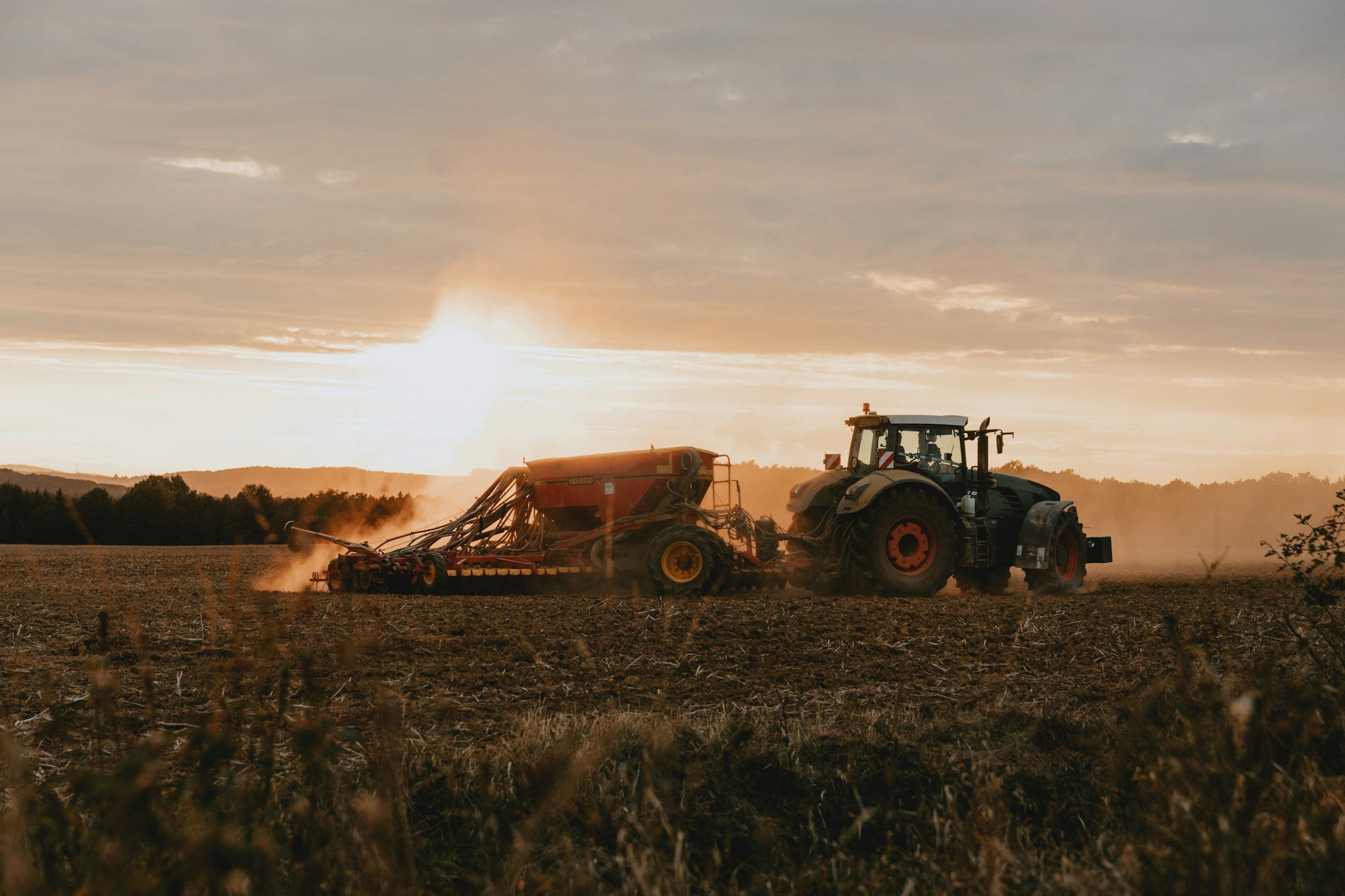 Trator com implemento trabalhando no campo ao entardecer